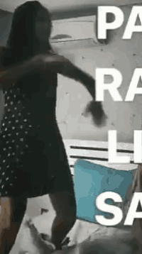 a woman in a black dress is dancing on a bed in front of a blue pillow .