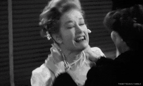 a black and white photo of a woman laughing while another woman holds her face .