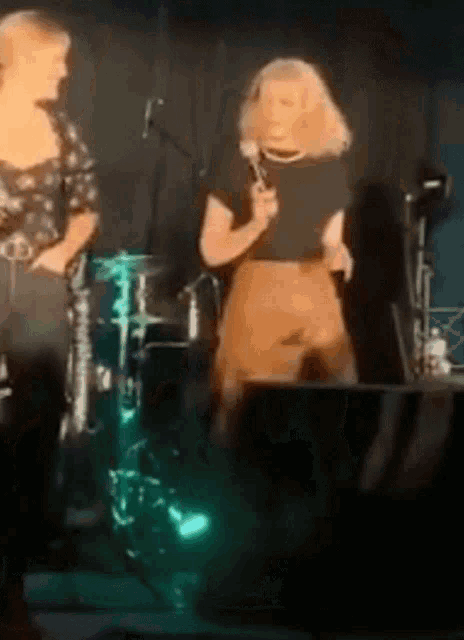 a woman singing into a microphone while standing next to a drum set