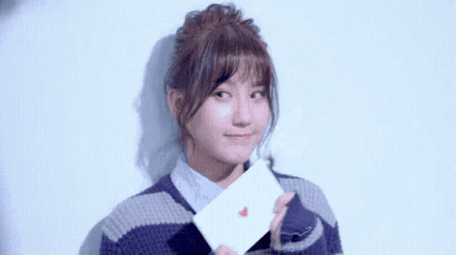 a woman in a striped sweater is holding an envelope with a red heart on it .