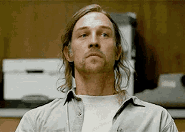 a man with long hair and a beard is wearing a white shirt and looking up .