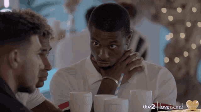 a group of men are sitting at a table with itv 2 love island written in the corner