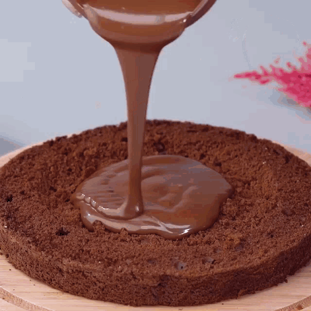 chocolate is being poured onto a cake on a wooden cutting board
