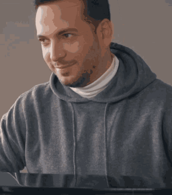 a man in a grey hoodie is smiling while sitting at a piano