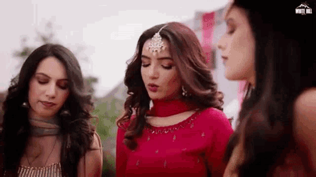 a group of women are standing next to each other in a room . one of the women is wearing a red dress .