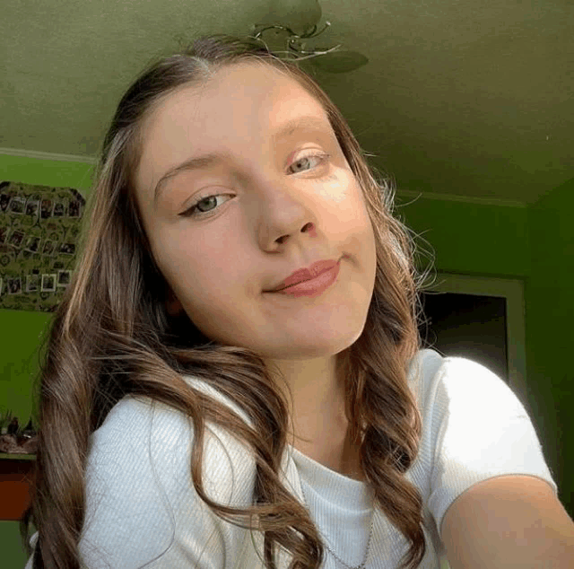 a girl in a white shirt is taking a selfie in front of a green wall