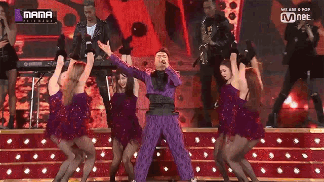 a man in a purple suit is singing into a microphone on a stage surrounded by women