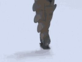 a woman wearing a gray coat and green boots is walking down a runway .
