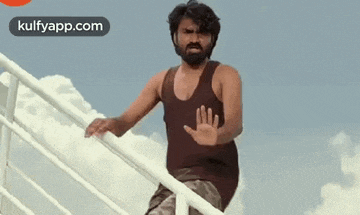 a man with a beard is standing on a railing with his hand out .
