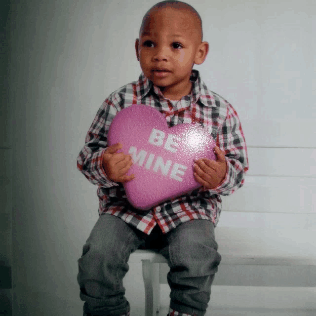 a young boy is holding a heart that says be mine