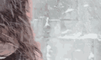 a woman with long hair is standing in front of a brick wall .