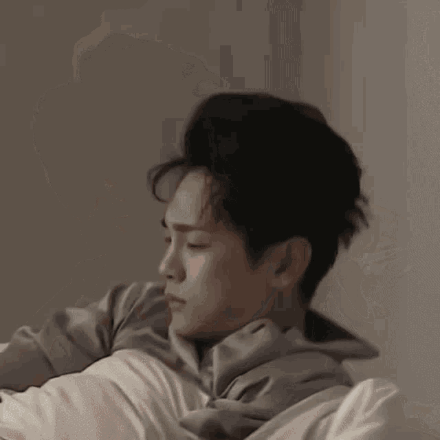 a young man is laying on a bed with a pillow and a blanket .