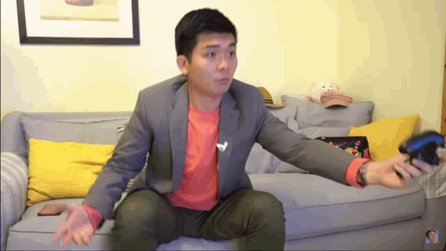 a man in a suit is sitting on a couch holding a game controller