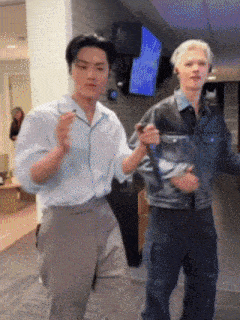 a man in a denim jacket is holding a microphone while dancing with another man
