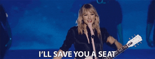taylor swift is singing into a microphone while holding a guitar and saying `` i 'll save you a seat ''
