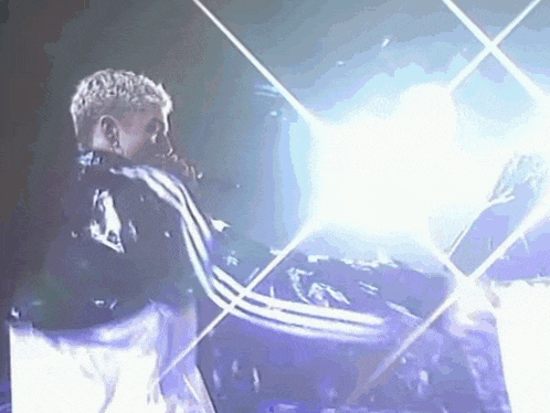 a man in a black adidas jacket is singing into a microphone on stage