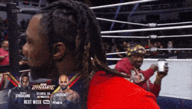 a man with dreadlocks is sitting in a wrestling ring next to a poster that says new dynamite