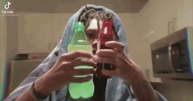 a man with dreadlocks is holding two bottles of soda in his hands .