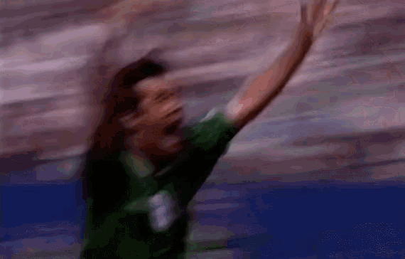 a blurry picture of a person in a green shirt raising their arms in the air .