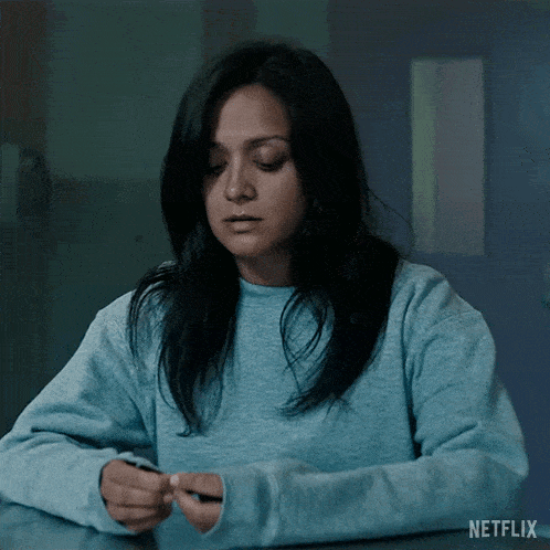 a woman in a blue sweater is sitting at a table with a netflix logo on the bottom right