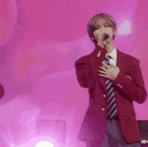 a man singing into a microphone with a pink background