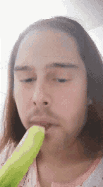 a man with long hair and a beard is licking a green banana .