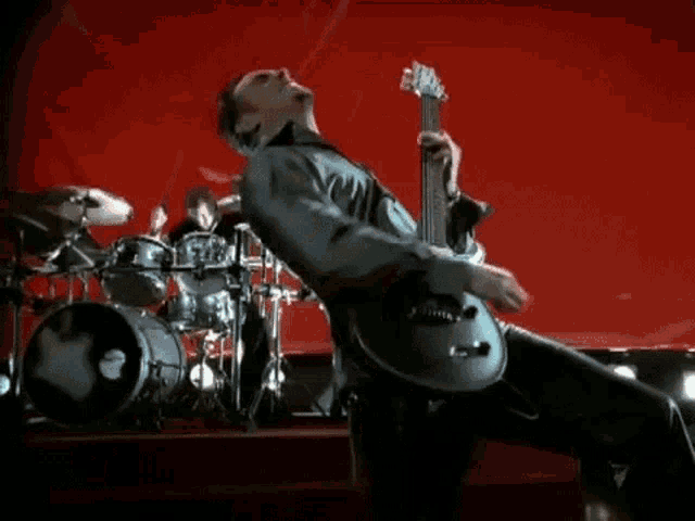 a man is playing a guitar on a stage with a drummer in the background .