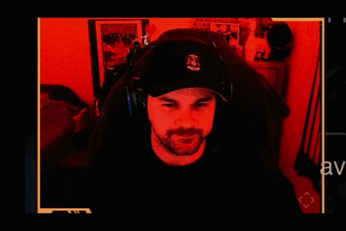 a man wearing a hat and headphones looks at the camera in a dark room