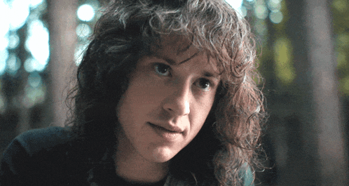 a man with long curly hair looks at the camera