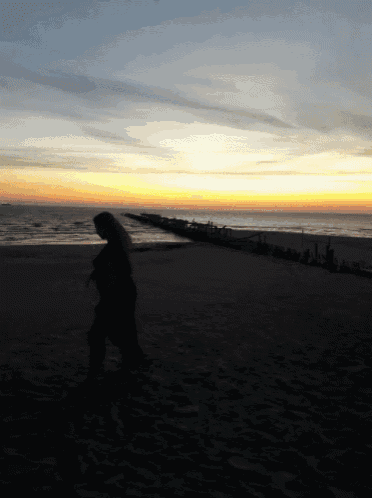 a person walking on a beach at sunset