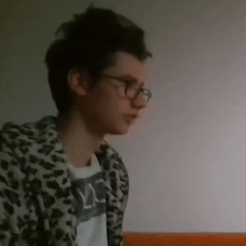 a young man wearing glasses and a leopard print jacket looks to the side