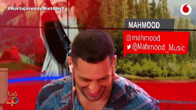 a man wearing headphones is smiling in front of a sign that says mahmood on it