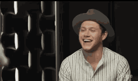 a man wearing a hat is laughing while sitting in front of a wall .