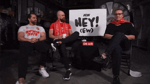 three men sit in front of a sign that says " hey "