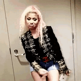 a woman with pink hair is standing in front of a door and making a face