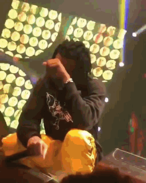 a man wearing a black hoodie and yellow pants is sitting on a stage holding a microphone ..