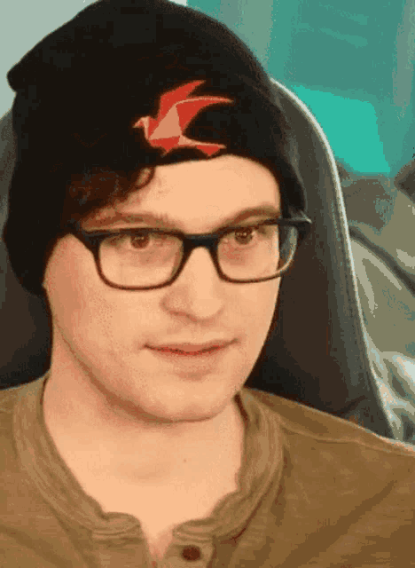 a man wearing glasses and a black beanie has a red bird on it