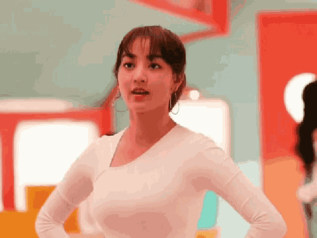a woman in a white shirt is standing with her hands on her hips and looking at the camera .