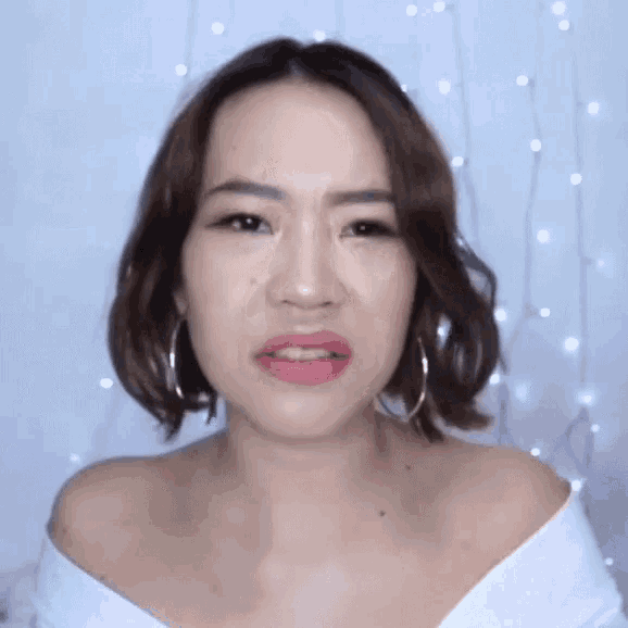 a woman wearing hoop earrings and a white top is making a funny face .