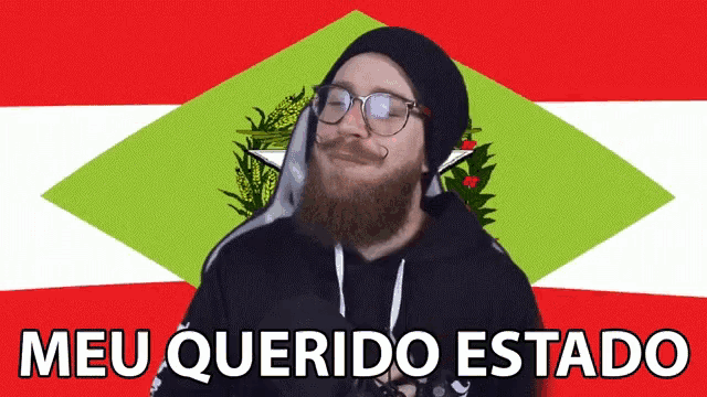 a man with glasses and a beard is standing in front of a green and red flag with the words meu querido estado below him