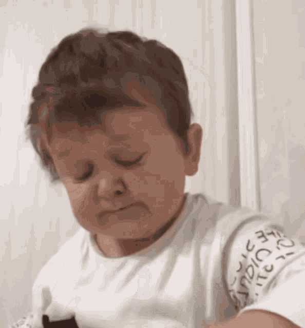 a baby is making a sad face while wearing a white shirt with the word nike on it .