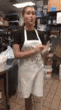 a woman in an apron is standing in a kitchen holding a plate .