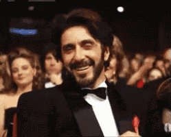 a man in a tuxedo and bow tie is smiling in front of a crowd of people