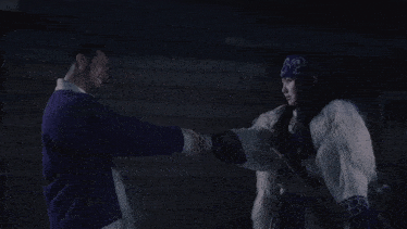 a man in a purple jacket and a woman in a white fur coat are standing next to each other in the dark .