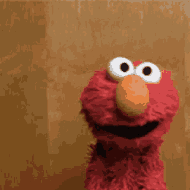 elmo from sesame street is looking at the camera and smiling .