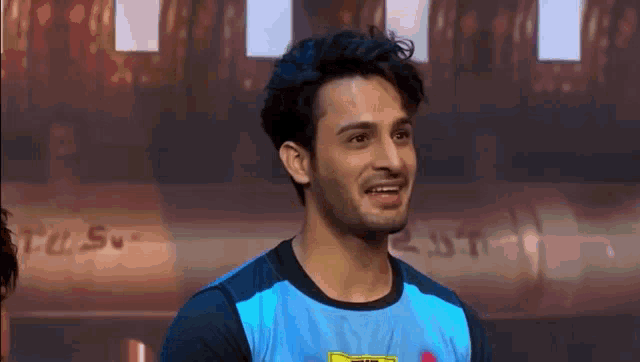 a man in a blue shirt is standing in front of a wall and smiling .