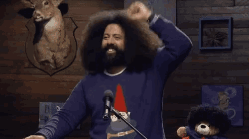 a man with a beard and long hair is standing in front of a microphone in front of a stuffed animal .