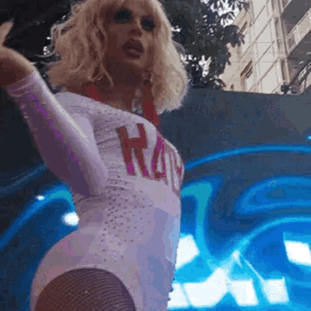a drag queen is wearing a white leotard and fishnet stockings while dancing on a stage .