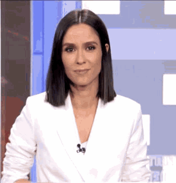a woman in a white jacket is standing in front of a microphone in a news studio .