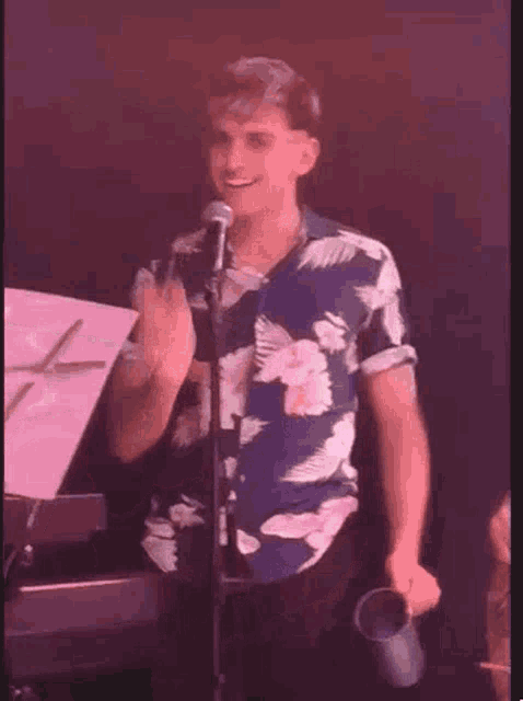 a man in a floral shirt is holding a microphone and a piece of paper .
